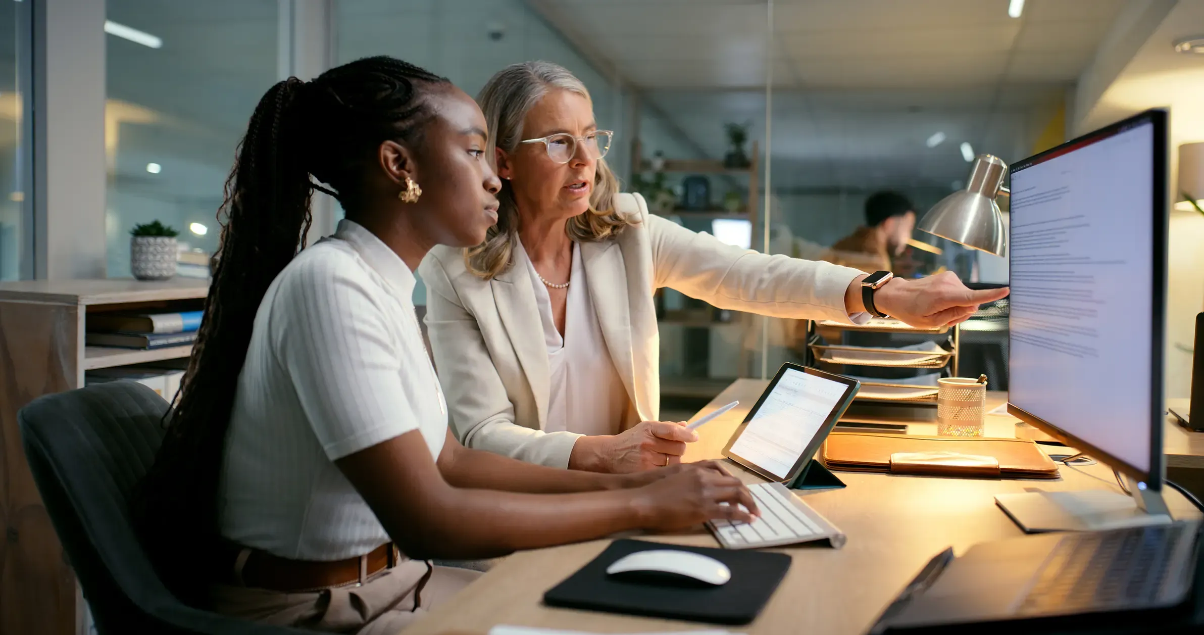 Mentor/manager helping intern accountant to track financial payments at a desk.
