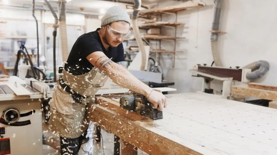 Young craftsperson working on wood is focused while wood chips fly from his work.