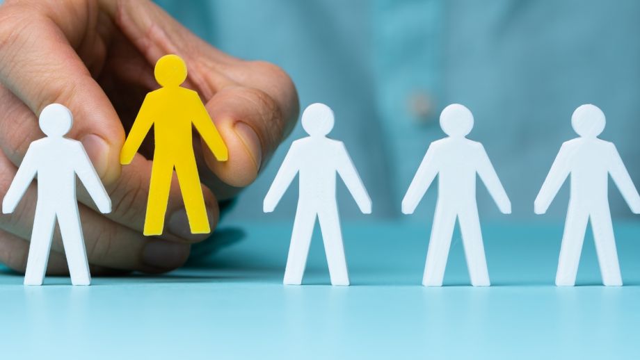Hand choosing yellow figure from among white ones, representing profiles.